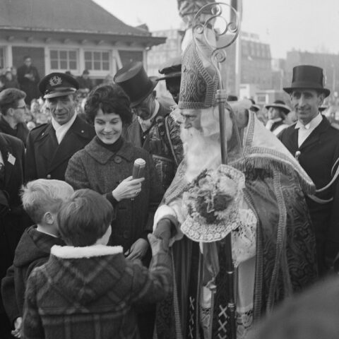 Sinterklaas op paard tijdens de intocht van 1962, zwart wit foto. Op de foto staat Mies Bouwman bij sinterklaas om