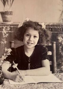 Oude foto van een jong kint met schrift aan tafel.